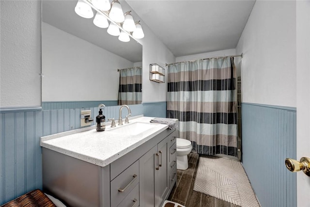 full bath featuring a shower with shower curtain, toilet, a wainscoted wall, vanity, and wood finish floors