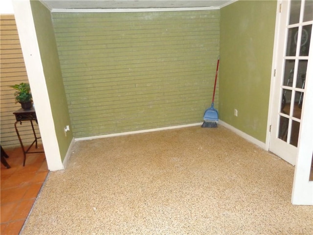 unfurnished room with brick wall, ornamental molding, baseboards, and speckled floor