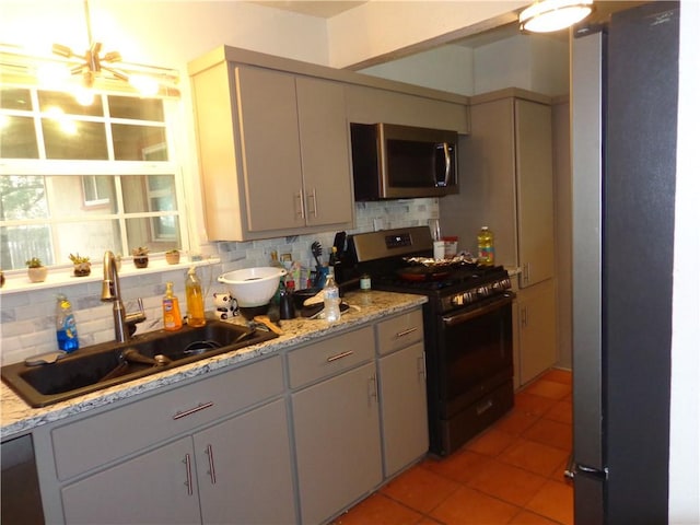 kitchen featuring light tile patterned floors, stainless steel appliances, tasteful backsplash, an inviting chandelier, and a sink