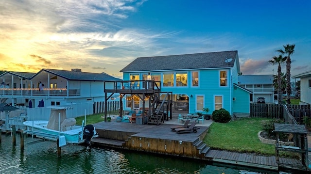 back house at dusk featuring a balcony, a patio, a yard, and a deck with water view