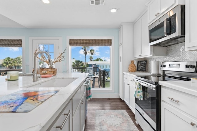 kitchen featuring stainless steel appliances, white cabinetry, sink, light stone countertops, and dark wood-type flooring