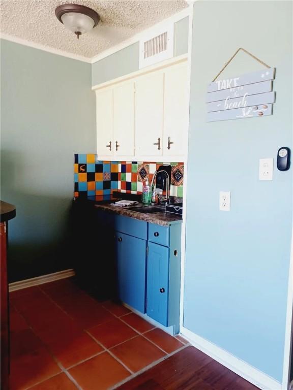 kitchen featuring white cabinets, sink, decorative backsplash, blue cabinetry, and a textured ceiling