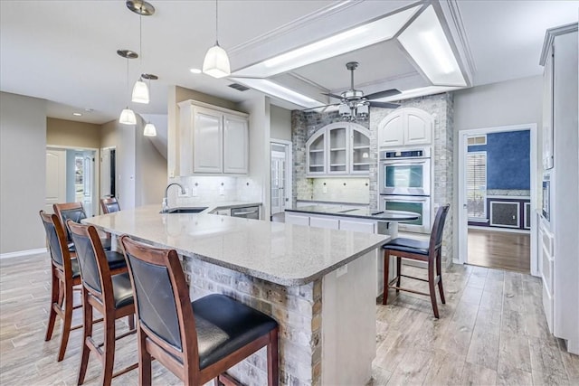 kitchen featuring kitchen peninsula, a kitchen breakfast bar, light wood-type flooring, stainless steel double oven, and decorative light fixtures