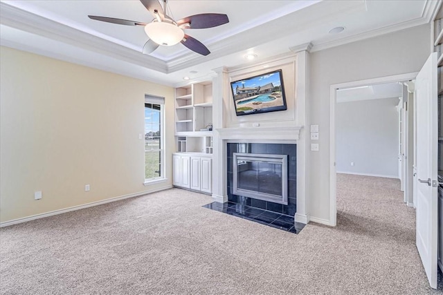 unfurnished living room featuring ceiling fan, a raised ceiling, crown molding, carpet floors, and a fireplace