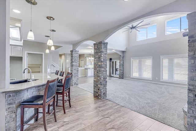 kitchen featuring light carpet, decorative columns, sink, decorative light fixtures, and a breakfast bar area