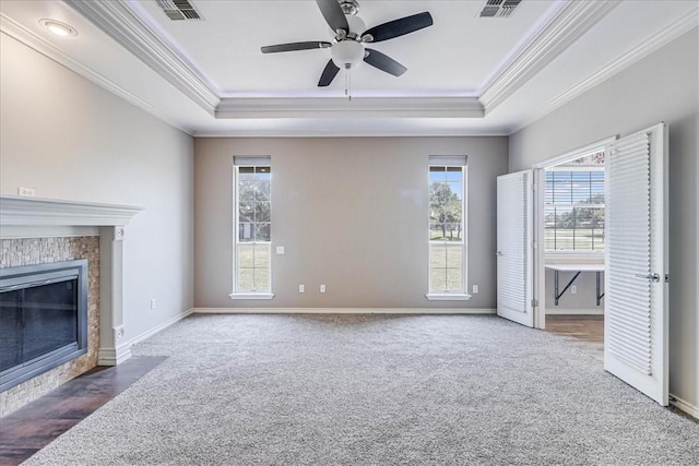 unfurnished living room featuring dark colored carpet, ceiling fan, a tiled fireplace, and a tray ceiling