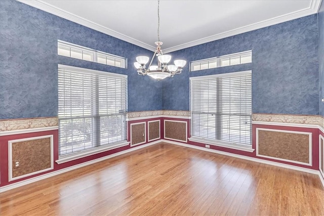 empty room with a wealth of natural light, ornamental molding, wood-type flooring, and a notable chandelier