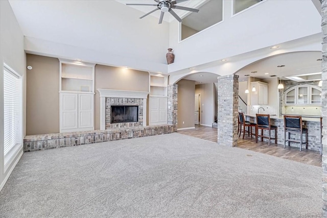 living room with ceiling fan, a towering ceiling, light carpet, and a brick fireplace