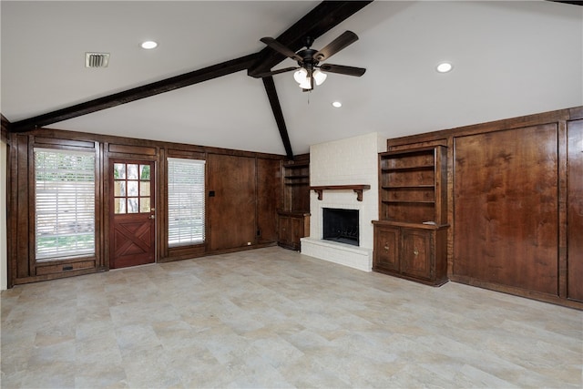 unfurnished living room featuring a fireplace, ceiling fan, wooden walls, and vaulted ceiling with beams