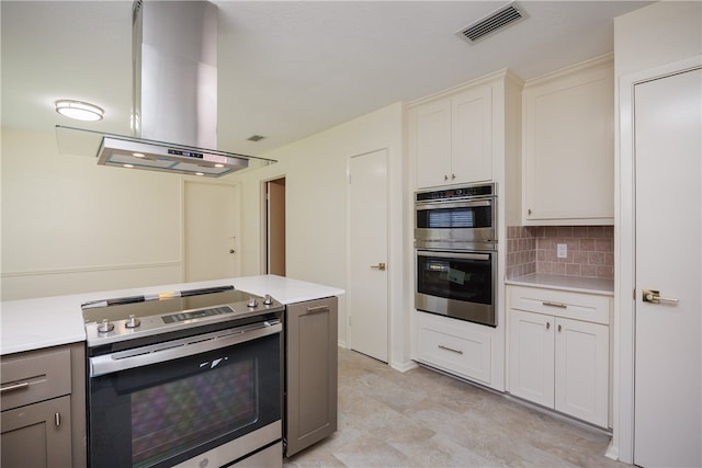 kitchen with white cabinetry, island range hood, decorative backsplash, and appliances with stainless steel finishes