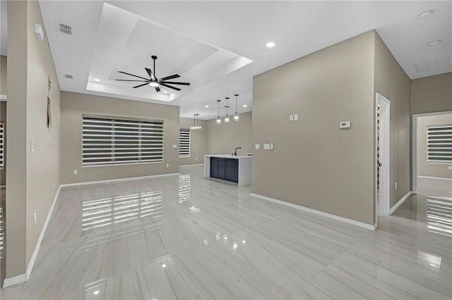 unfurnished living room featuring sink, ceiling fan, and a tray ceiling