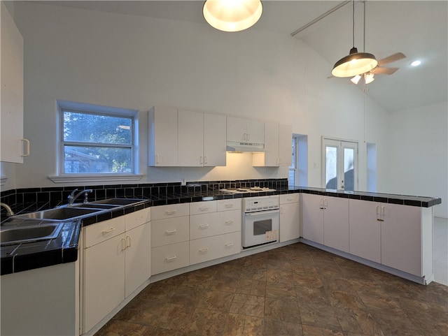 kitchen featuring tile countertops, white appliances, high vaulted ceiling, kitchen peninsula, and white cabinetry