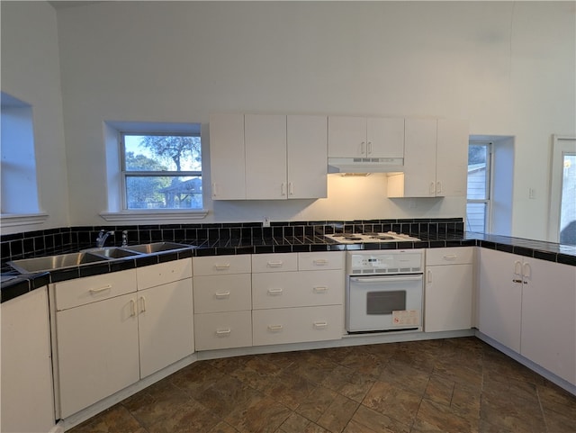 kitchen with a towering ceiling, white appliances, sink, white cabinetry, and tile counters