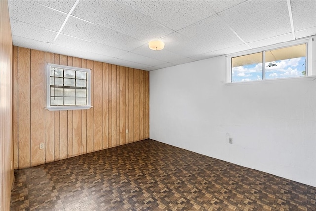 spare room featuring wood walls, a drop ceiling, and dark parquet flooring