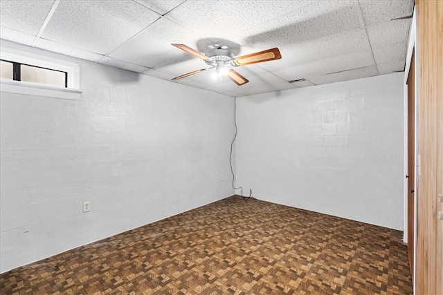 basement with ceiling fan, dark parquet flooring, and a drop ceiling