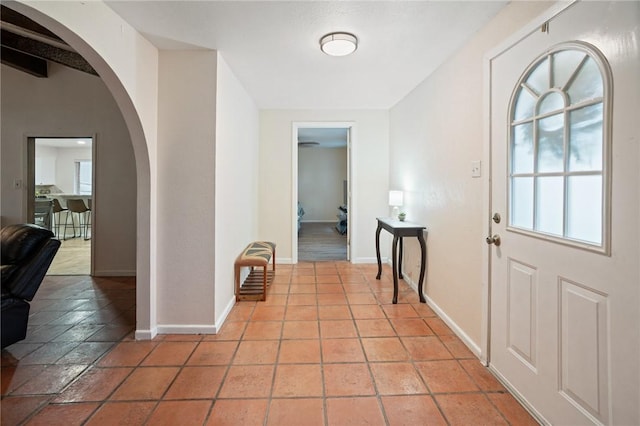 entryway featuring arched walkways, light tile patterned floors, baseboards, and a healthy amount of sunlight