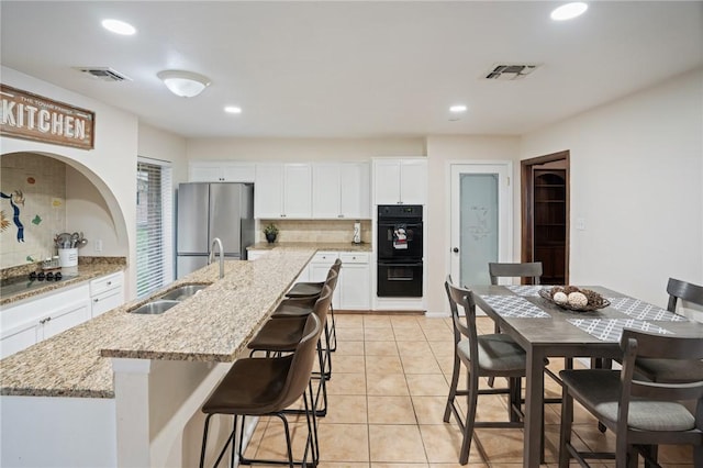 kitchen with visible vents, white cabinets, a kitchen island with sink, black appliances, and a sink