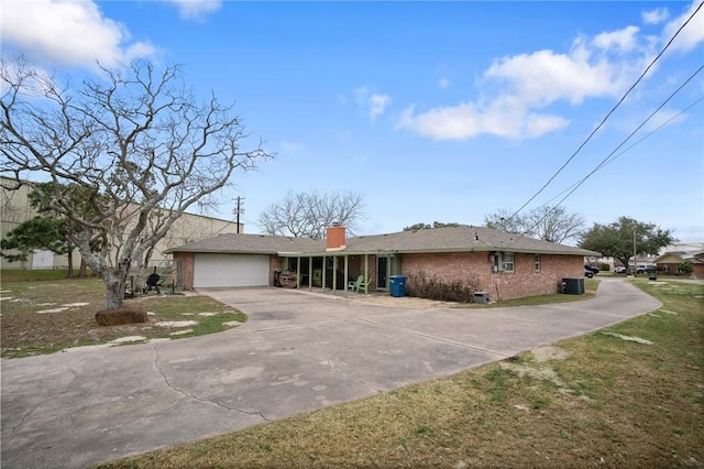 single story home with a garage, brick siding, concrete driveway, a chimney, and a front yard