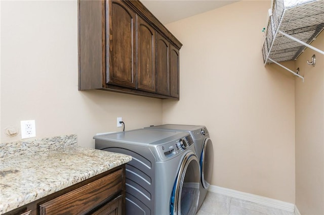 clothes washing area featuring cabinet space, light tile patterned floors, baseboards, and washing machine and clothes dryer