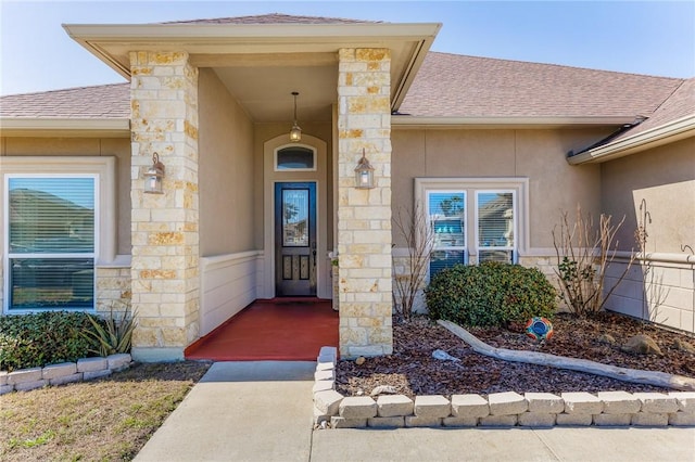 doorway to property featuring stone siding, roof with shingles, and stucco siding