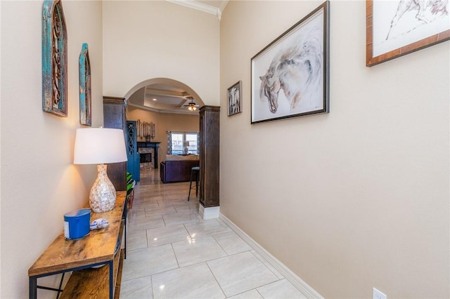 corridor with light tile patterned flooring, baseboards, arched walkways, and ornamental molding