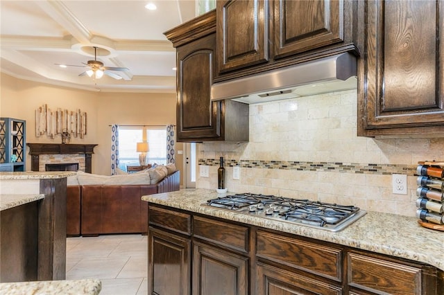 kitchen with ceiling fan, under cabinet range hood, a fireplace, dark brown cabinets, and stainless steel gas stovetop