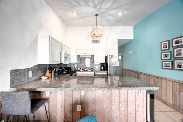 kitchen with appliances with stainless steel finishes, stone counters, wainscoting, and a peninsula