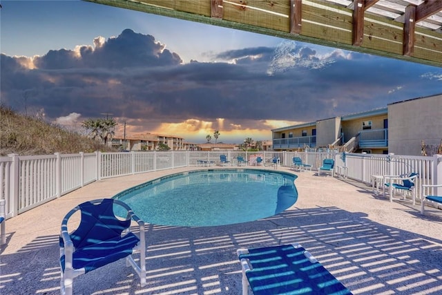 pool at dusk featuring a patio area, fence, and a community pool