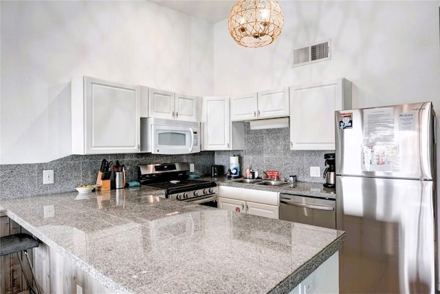 kitchen with visible vents, appliances with stainless steel finishes, white cabinets, a sink, and a peninsula