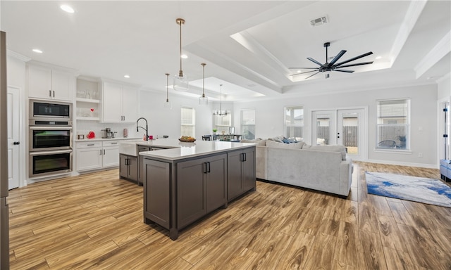 kitchen with pendant lighting, a kitchen island with sink, a tray ceiling, white cabinets, and built in microwave