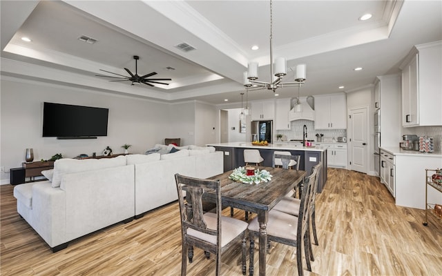 dining area featuring crown molding, a tray ceiling, ceiling fan with notable chandelier, and light hardwood / wood-style floors