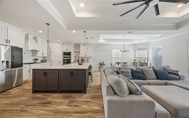 kitchen featuring premium range hood, white cabinetry, stainless steel appliances, a raised ceiling, and a spacious island