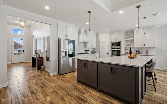 kitchen featuring a large island, premium range hood, stainless steel appliances, white cabinets, and decorative light fixtures