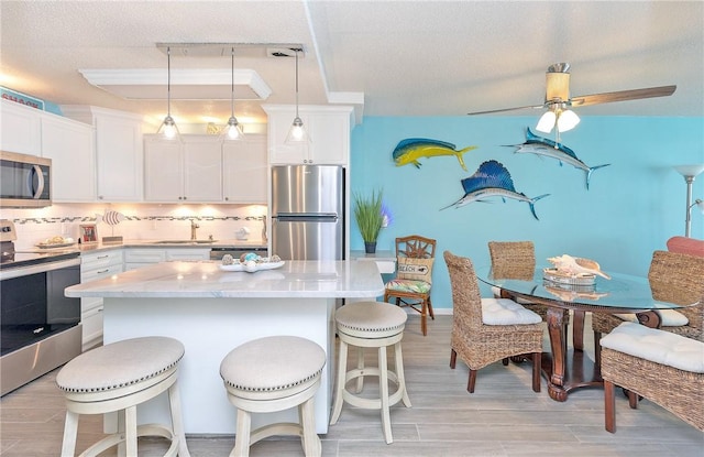 14810 Windward Dr Unit 203, Corpus Christi, TX 78418 - kitchen featuring appliances with stainless steel finishes, a kitchen breakfast bar, decorative backsplash, white cabinetry, and a textured ceiling