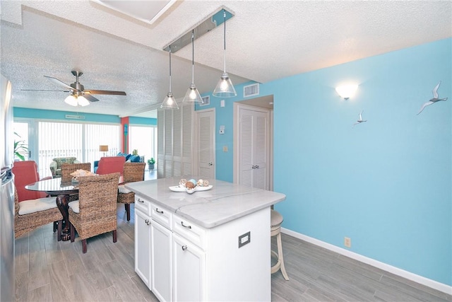 14810 Windward Dr Unit 203, Corpus Christi, TX 78418 - kitchen with a textured ceiling, light wood-style flooring, a kitchen bar, white cabinetry, and a center island