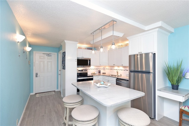 14810 Windward Dr Unit 203, Corpus Christi, TX 78418 - kitchen featuring appliances with stainless steel finishes, a textured ceiling, white cabinets, a breakfast bar, and tasteful backsplash