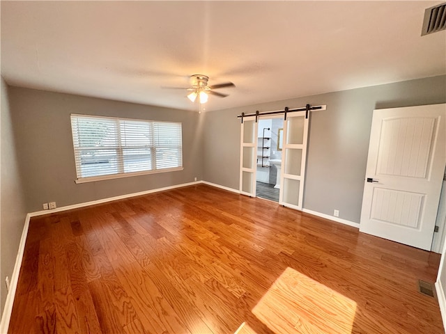 spare room featuring a barn door, hardwood / wood-style flooring, and ceiling fan