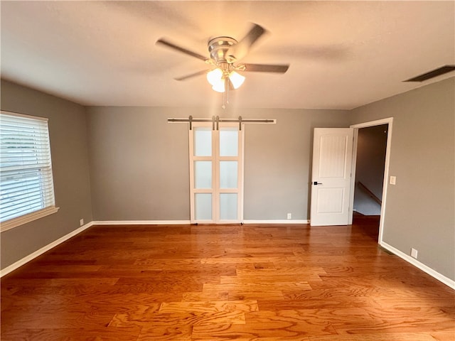 spare room with a barn door, ceiling fan, and hardwood / wood-style flooring