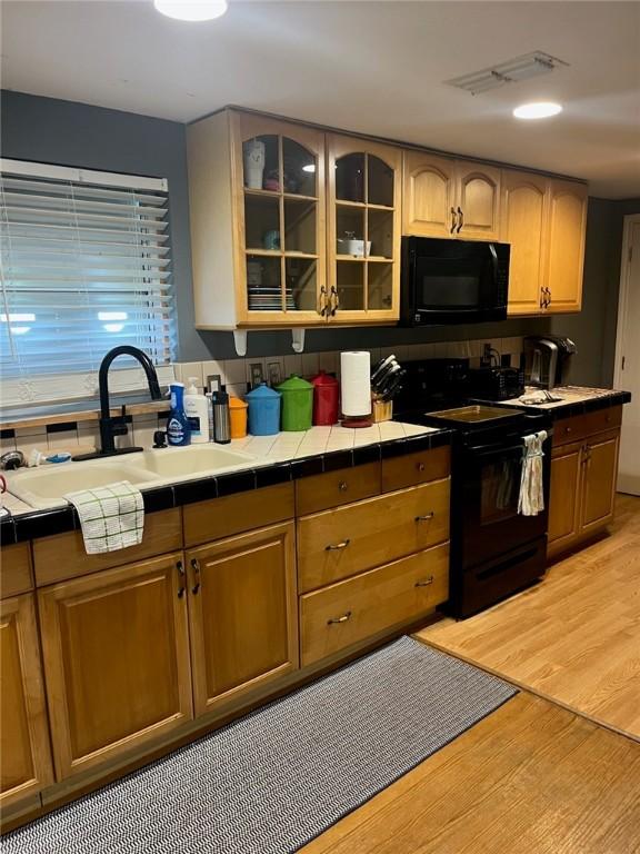 66 Redfish Dr, Rockport, TX 78382 - kitchen featuring black appliances, tile counters, light wood-style flooring, and glass insert cabinets