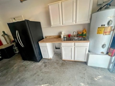 kitchen with white cabinetry, water heater, black fridge, and sink