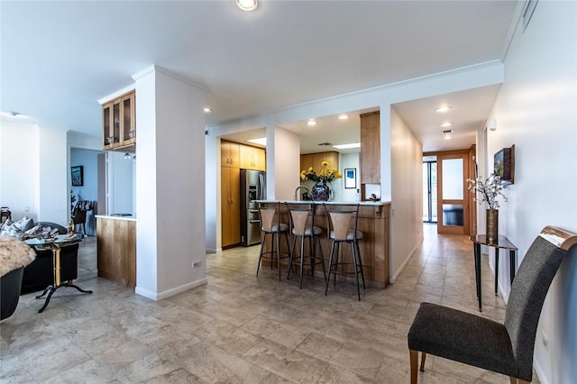 kitchen featuring crown molding, a kitchen breakfast bar, stainless steel fridge, a peninsula, and baseboards