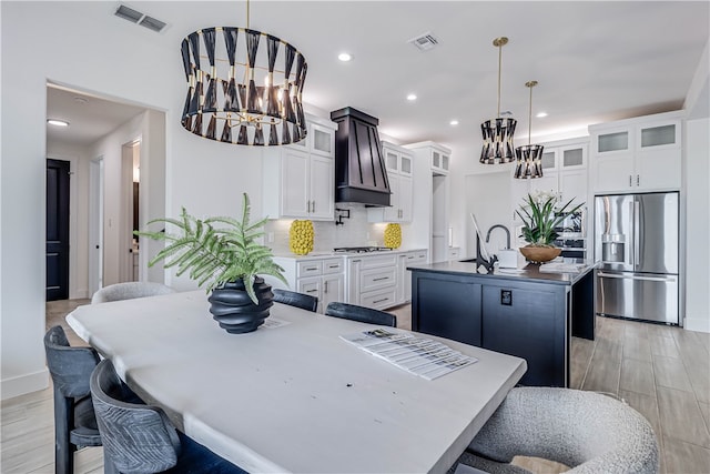 kitchen with pendant lighting, appliances with stainless steel finishes, a center island with sink, and white cabinets