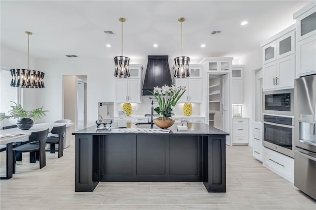 kitchen featuring white cabinets, appliances with stainless steel finishes, decorative light fixtures, and a kitchen island with sink