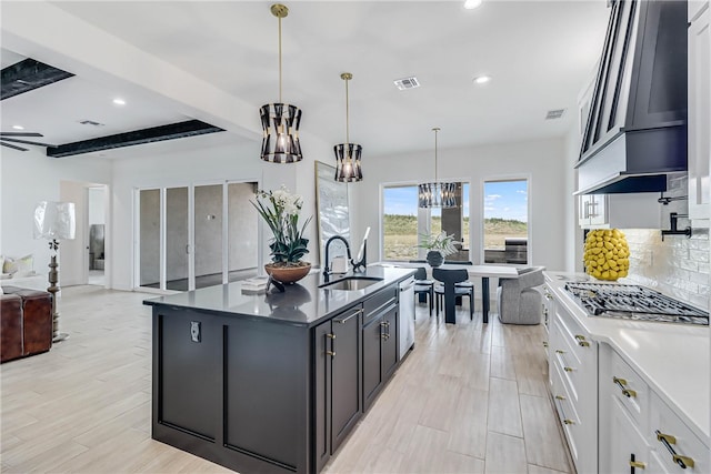 kitchen with a center island with sink, white cabinetry, decorative light fixtures, beam ceiling, and sink