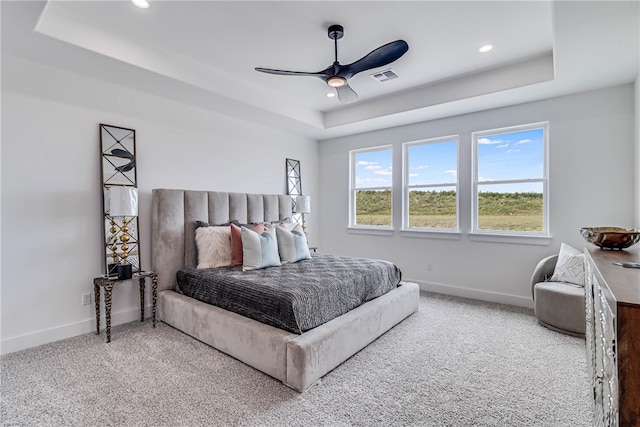 carpeted bedroom with ceiling fan and a tray ceiling