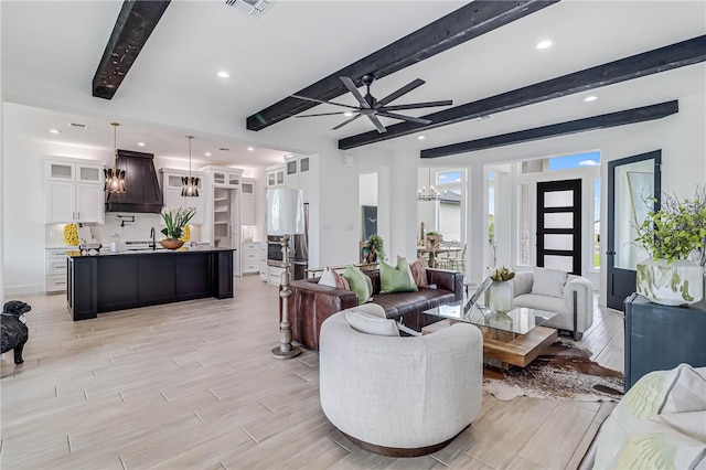 living room featuring ceiling fan, beamed ceiling, sink, and light wood-type flooring