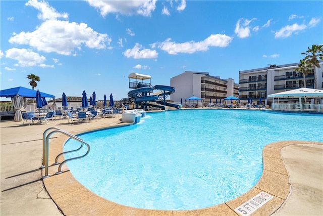 pool featuring a water slide, a patio area, and fence