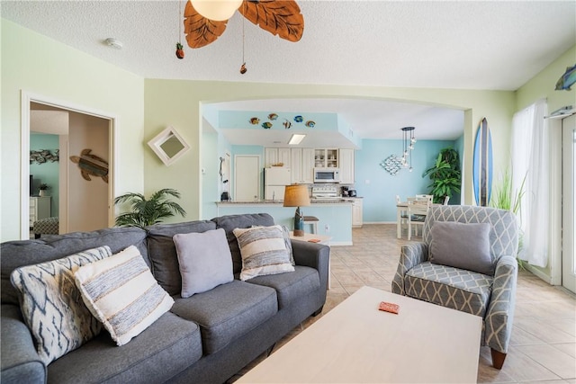 living room with light tile patterned floors, ceiling fan, baseboards, and a textured ceiling