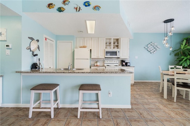 kitchen with light stone counters, a breakfast bar, light tile patterned flooring, white appliances, and a peninsula