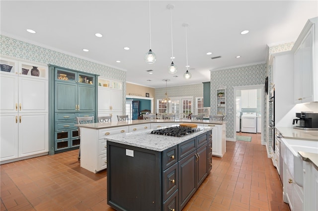 kitchen with kitchen peninsula, hanging light fixtures, stainless steel gas stovetop, crown molding, and a kitchen island